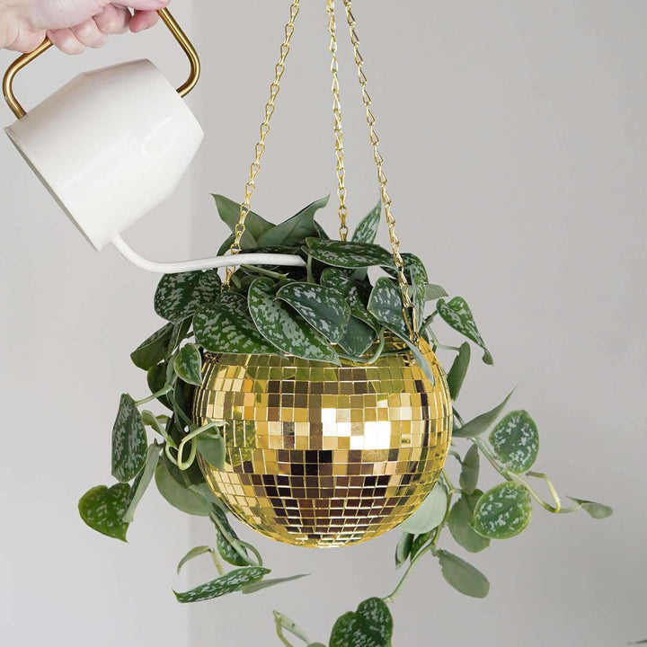 VibeCore Disco Ball Planter in gold, hanging with a reflective mirror-ball surface, holding a lush green plant being watered. This retro-inspired planter combines style and functionality, adding a vibrant, luxurious touch to your indoor or outdoor decor while showcasing plants in a playful and unique design.