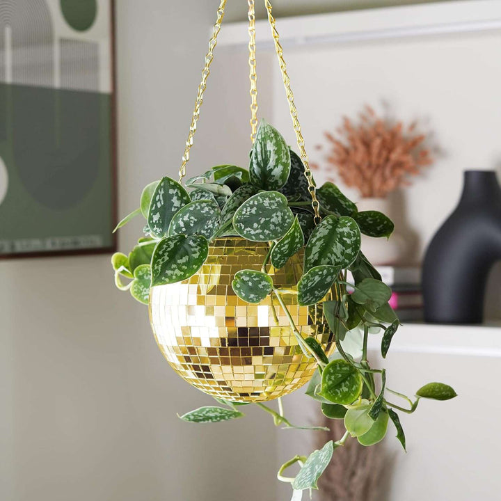 VibeCore Disco Ball Planter in gold, hanging gracefully with its reflective mirror-ball surface. This retro-inspired planter adds a touch of luxury and vibrancy to your space while showcasing plants in a stylish, eye-catching way. Perfect for enhancing the decor of your living room, bedroom, or office with a unique and playful design.