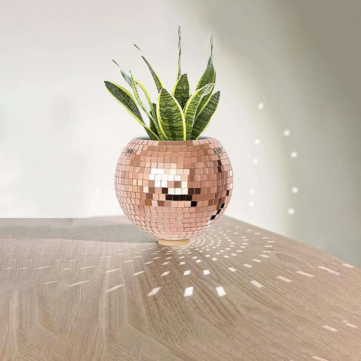 VibeCore Disco Ball Planter in rose pink, reflecting light off its shiny mirror-ball surface. This retro-inspired planter adds a playful, vibrant touch to your space while showcasing your plants. The reflective surface creates a stunning visual effect, perfect for brightening up your living room, bedroom, or office decor with a fun and unique vibe.