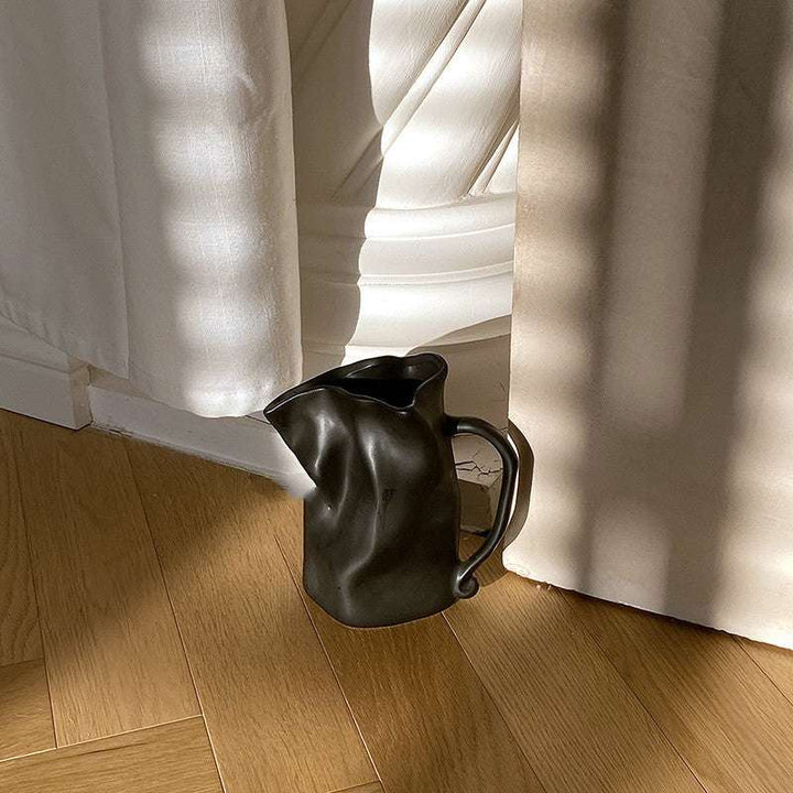 VibeCore Irregularly Folded Ceramic Vase in Black, elegantly displayed on the floor, showcasing its modern, sculptural design.