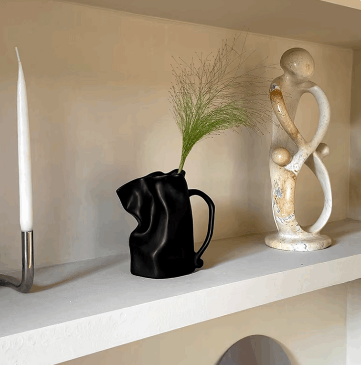 VibeCore Irregularly Folded Ceramic Vase in Black, displayed on a shelf, showcasing its minimalist design and modern sculptural appeal.