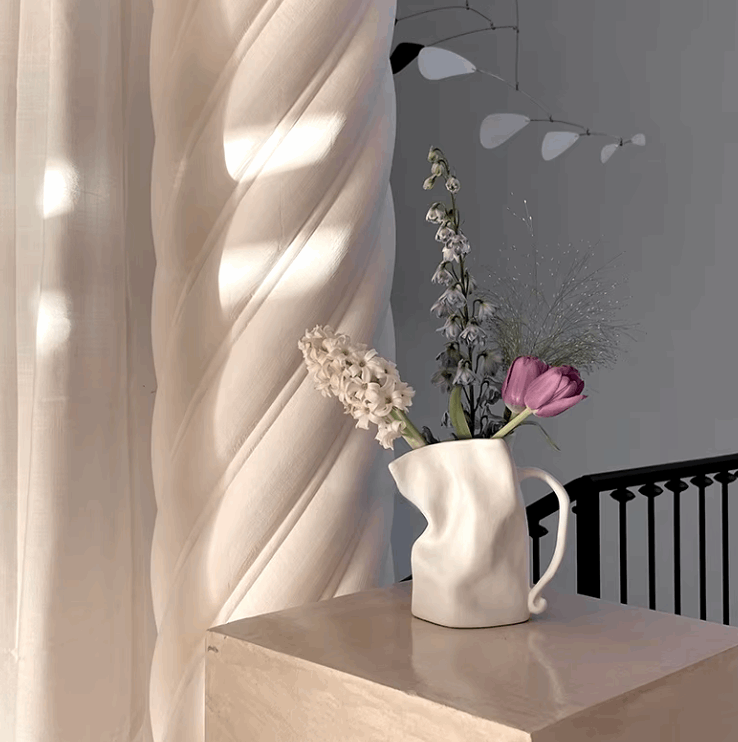 VibeCore Irregularly Folded Ceramic Vase in White, placed on a side table with dried flowers, showcasing its sculptural, minimalist design and modern elegance.