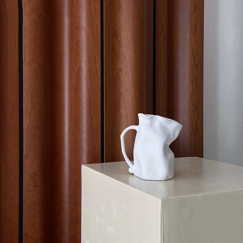 VibeCore Irregularly Folded Ceramic Vase in White, placed on a side table, highlighting its sculptural minimalist design and modern aesthetic.