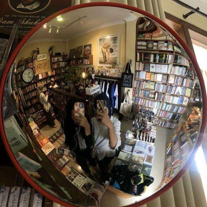 VibeCore Red Convex Traffic Mirror in bookstore, featuring a bold red frame and wide-angle lens for perfect selfies. This modern fish eye mirror adds a unique, urban vibe with its sleek convex design, offering a clear reflection and a trendy, industrial-style element to the bookstore's decor.