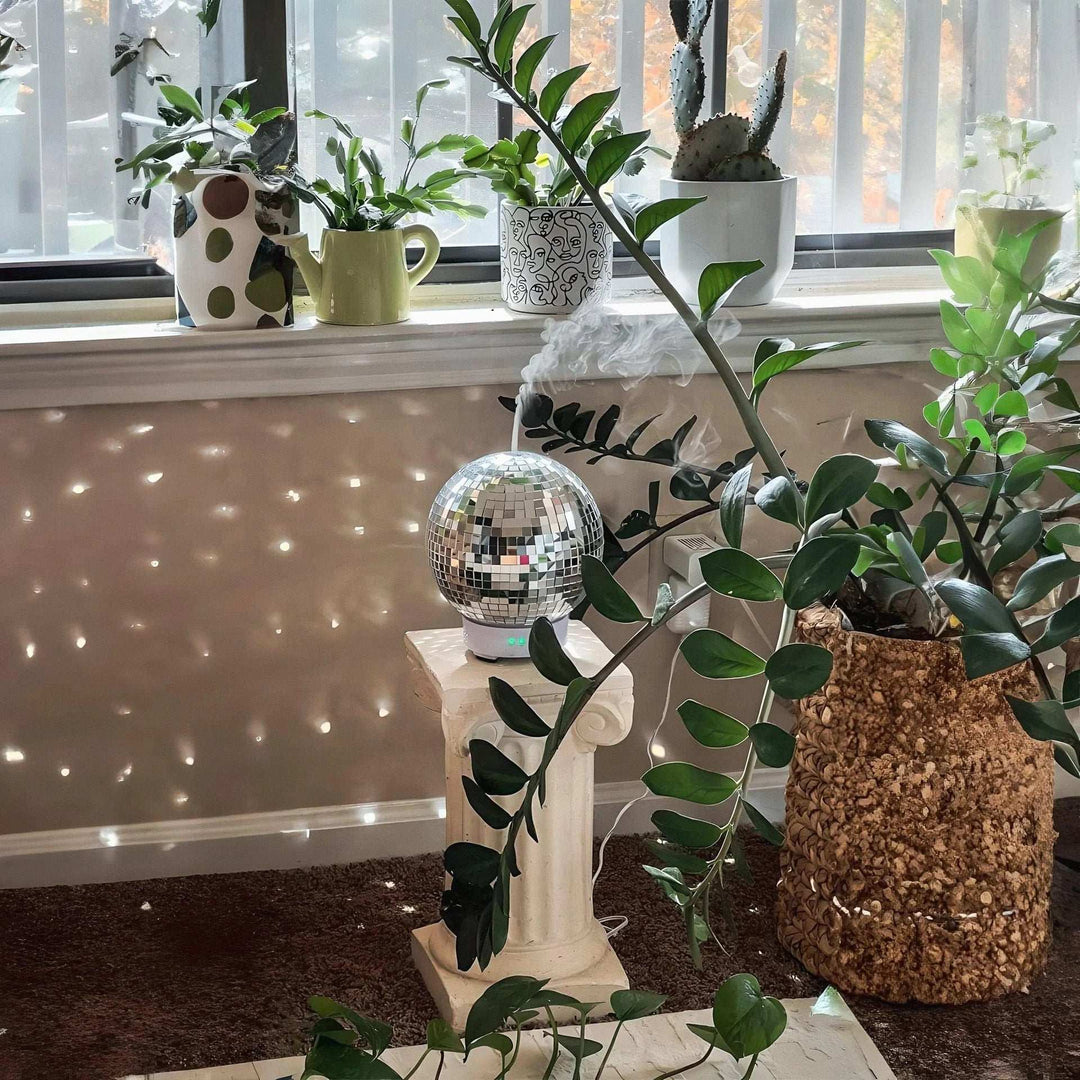 VibeCore Rotating Disco Ball Diffuser placed next to plants, casting vibrant light patterns and adding a playful, colorful ambiance to the room, blending modern decor with nature.