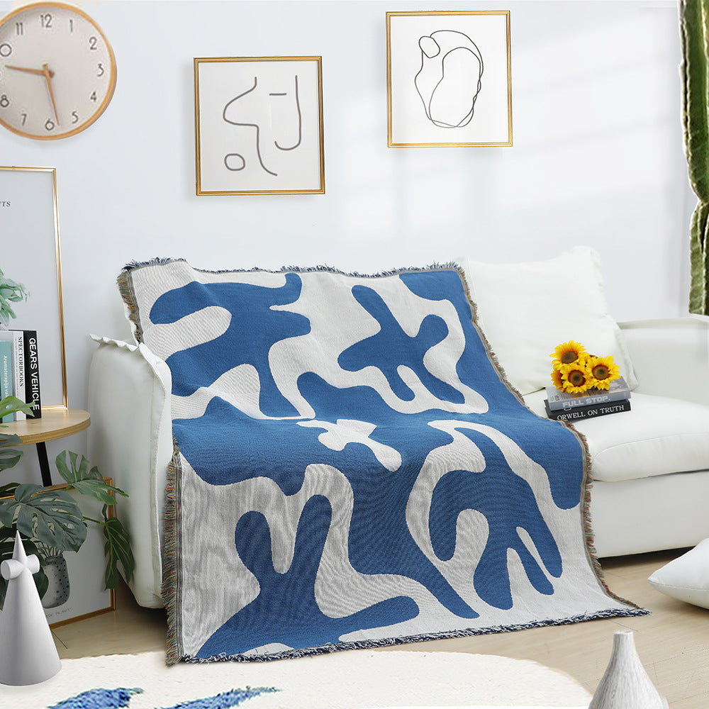 VibeCore Abstract Blue Coral Woven Blanket draped over couch, showcasing its dynamic coral-inspired design. Made from soft, breathable 100% combed cotton, this artistic blanket brings modern vibes and comfort to your living room, offering versatility with its reversible patterns for easy style changes.