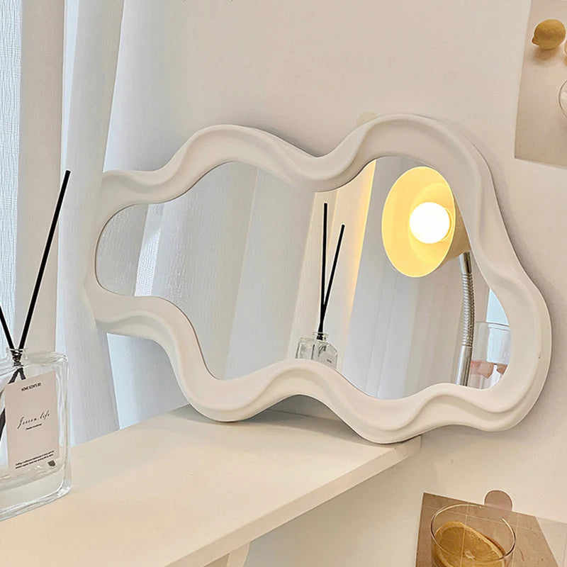 A chic abstract wall mirror with a light pink and white ripple design, elegantly placed on a shelf to add a touch of modern sophistication to your space.