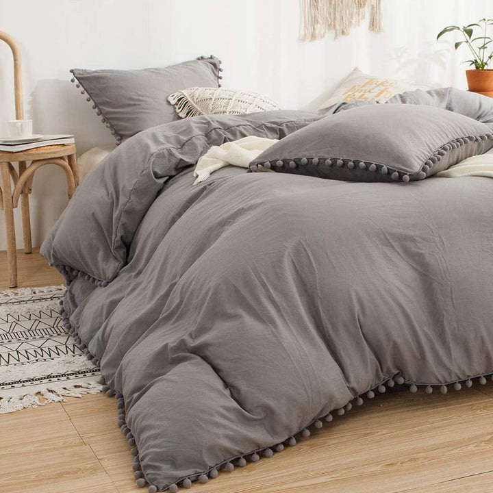 Aerial side view of the VibeCore Aesthetic PomPom Duvet Cover Set in light gray, showcasing the soft pom-pom accents along the edges. Made from soft, breathable fabric, this duvet set brings a playful, cozy touch to any bedroom or dorm, with a fresh, light aesthetic.