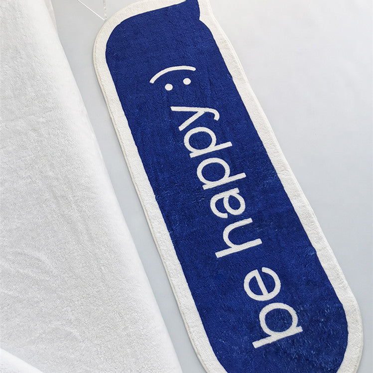 VibeCore Be Happy iMessage Accent Rug placed at the foot of a bed, adding a playful touch to the space. The vibrant blue design and soft, plush texture are visible, complementing the cozy bedroom decor. The non-slip backing ensures stability even in high-traffic areas.