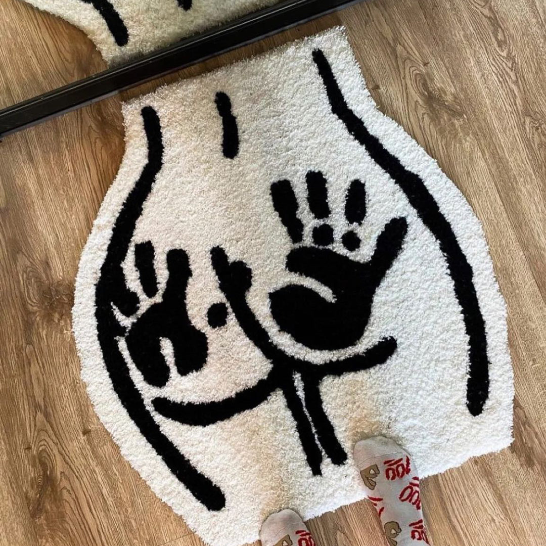 A playful VibeCore Booty Handprints Accent Rug in black and white, featuring bold handprint designs. Someone steps on the aesthetic rug, showcasing its soft, fluffy texture. Perfect for quirky decor, this unique rug adds personality to bedrooms, dorms, living rooms, or apartments. Its non-slip backing ensures safety while the durable material offers easy cleaning. Ideal as a fun rug, modern accent piece, or cool rug for urban and contemporary spaces.