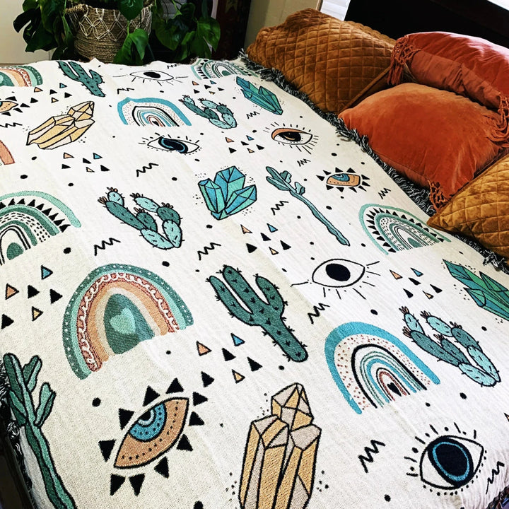 Close-up of the VibeCore Cactus & Crystals Woven Blanket on a bed, showcasing its vibrant cactus and crystal design and soft, breathable cotton texture.
