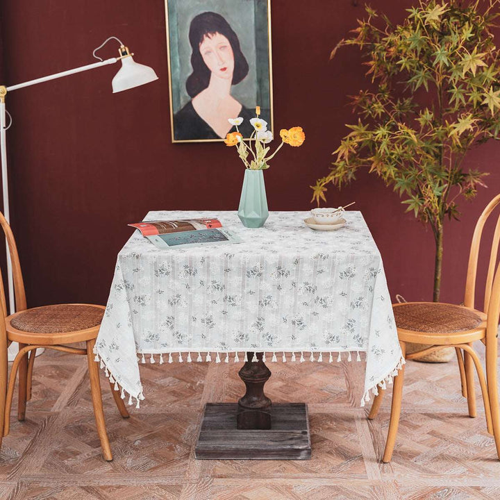 VibeCore Clove Flower Tassel Linen Tablecloth with delicate floral patterns and tassel edges, gracefully placed on a dining table in a cozy dining room, enhancing the space with an elegant touch.