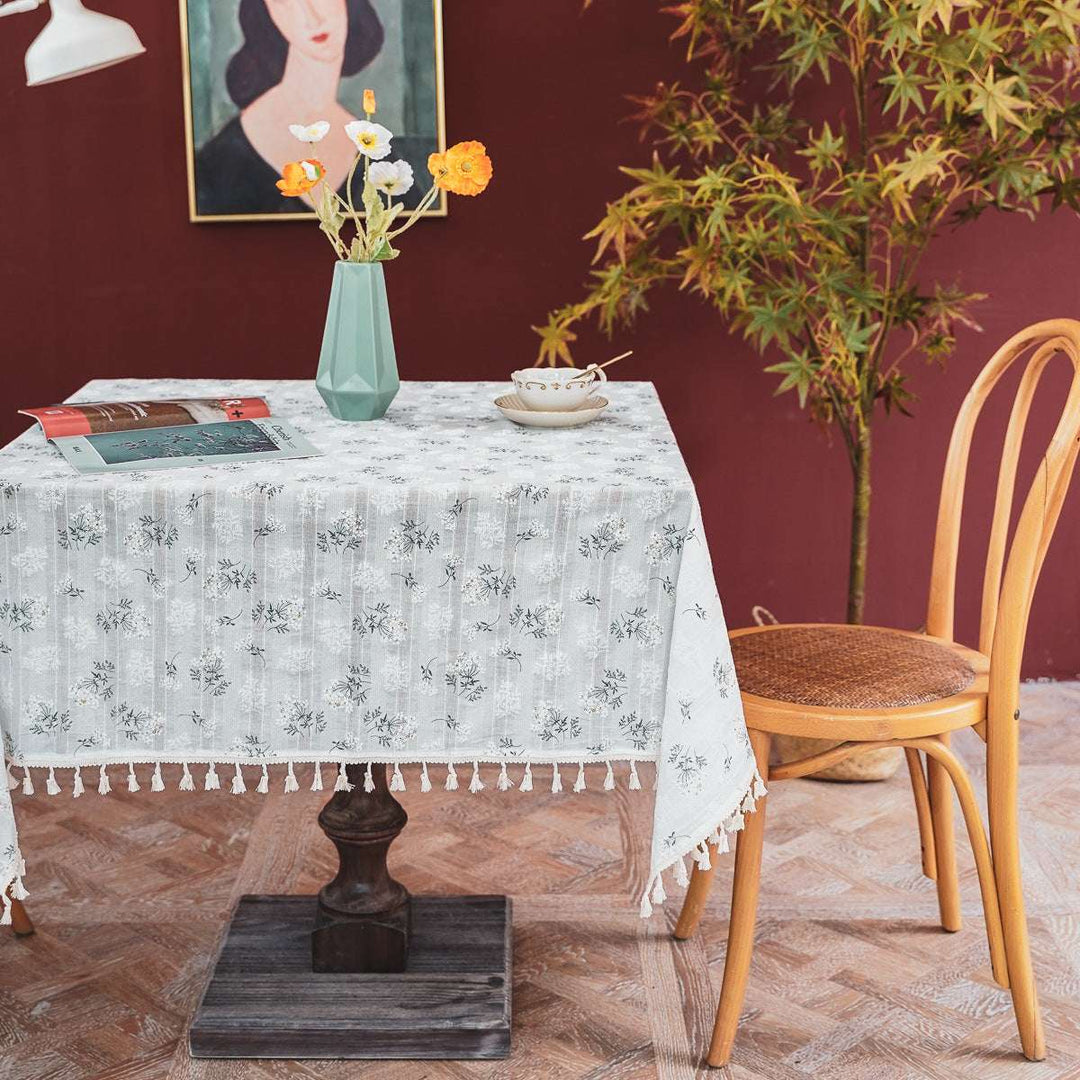 VibeCore Clove Flower Tassel Linen Tablecloth with floral patterns and tassel edges, elegantly draped on a table inside, adding a refined touch to the indoor dining setting.