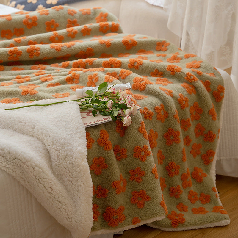 Close-up of an orange Delicate Florals Fleece Throw Blanket on the corner of a bed, showcasing its vibrant 70s-inspired floral design and soft coral fleece texture. A cozy, retro touch for your bedroom.