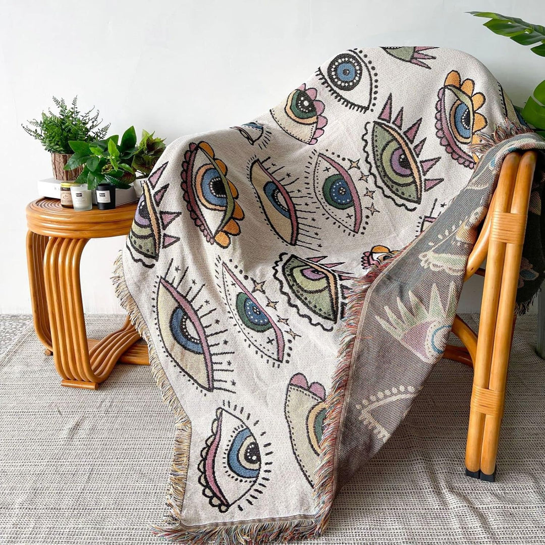 VibeCore Eternal Gaze Woven Blanket draped over chair, featuring an intriguing and bold design. Made from soft, breathable 100% combed cotton, it adds vibrant energy, mystique, and style to your space.