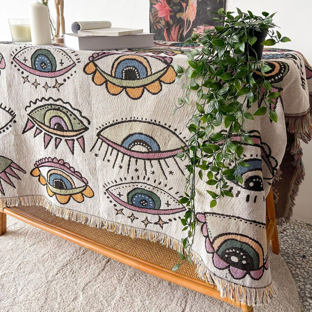 VibeCore Eternal Gaze Woven Blanket on table, showcasing its intriguing and bold design. Made from soft, breathable 100% combed cotton, it adds depth, mystique, and vibrant energy to your space with its unique pattern.