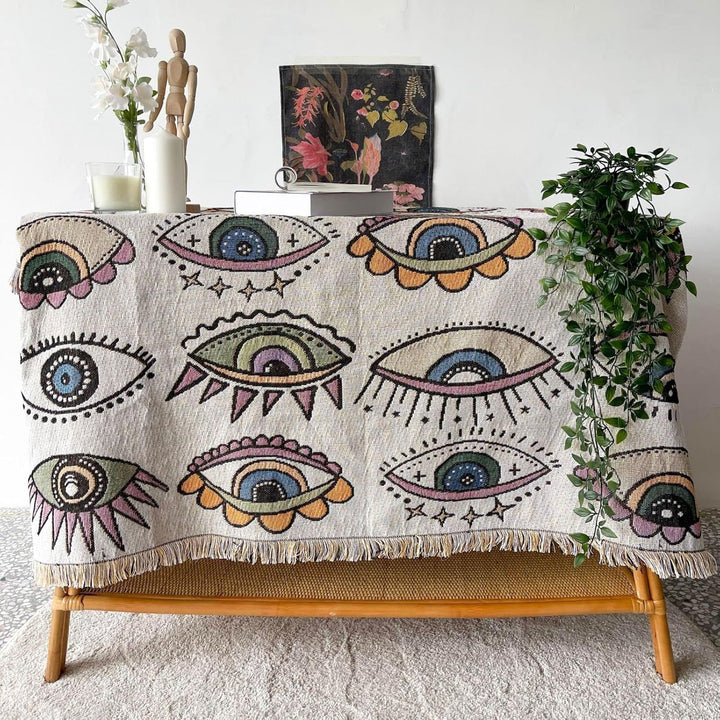 VibeCore Eternal Gaze Woven Blanket on table as tablecloth, featuring a captivating and bold design. Crafted from soft, breathable 100% combed cotton, it adds a touch of mystique, vibrant energy, and artistic flair to your dining or living space.