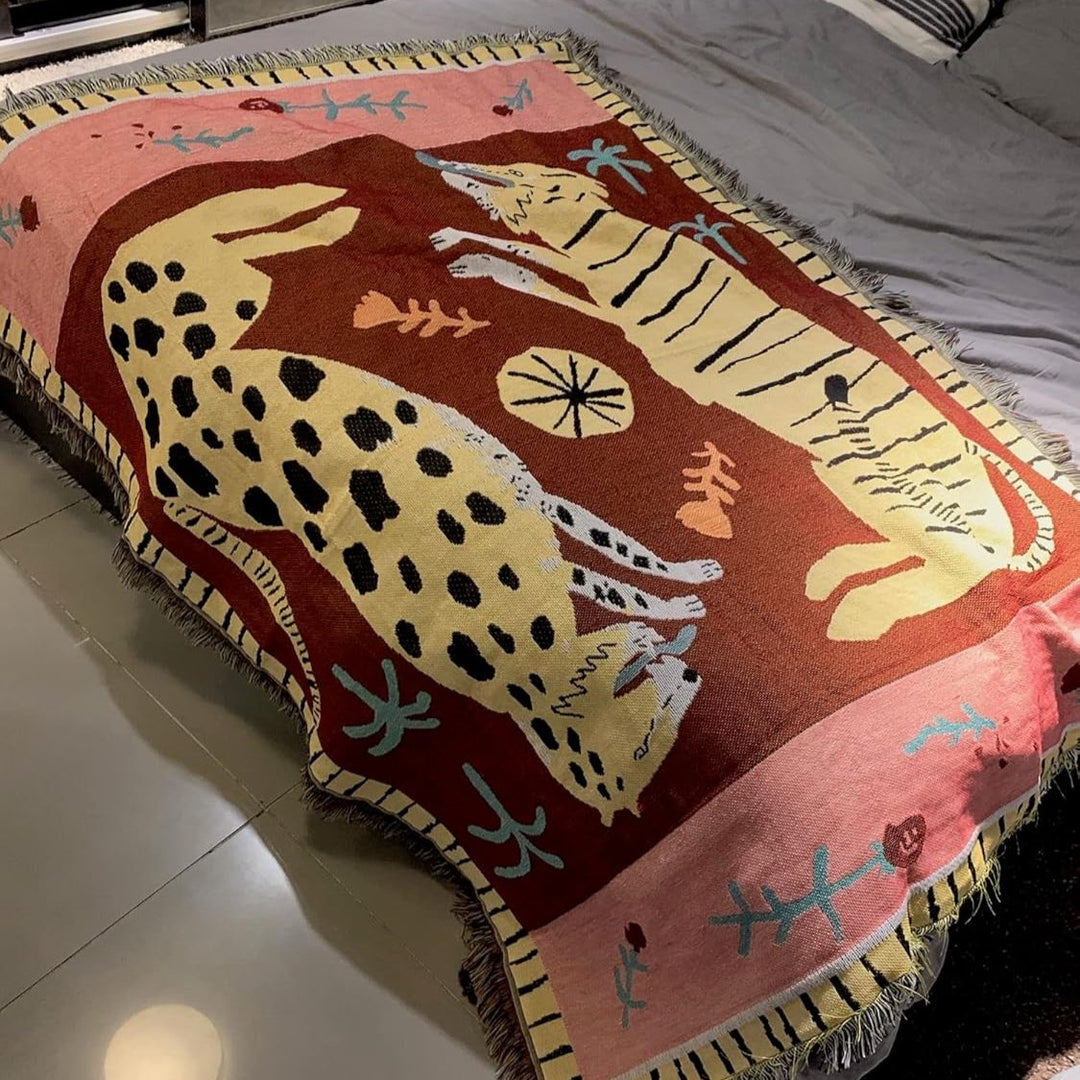 VibeCore Feline Power Woven Blanket draped on bed, featuring a bold jungle-inspired design and made of soft, breathable 100% cotton.
