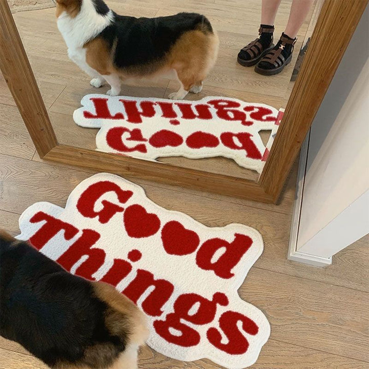 Aesthetic red "Good Things Accent Rug" displayed on the floor in front of a mirror, with a corgi sitting on it. Featuring a motivational Y2K message, this soft, plush rug adds warmth and positivity to the space while providing comfort and safety with its non-slip backing.