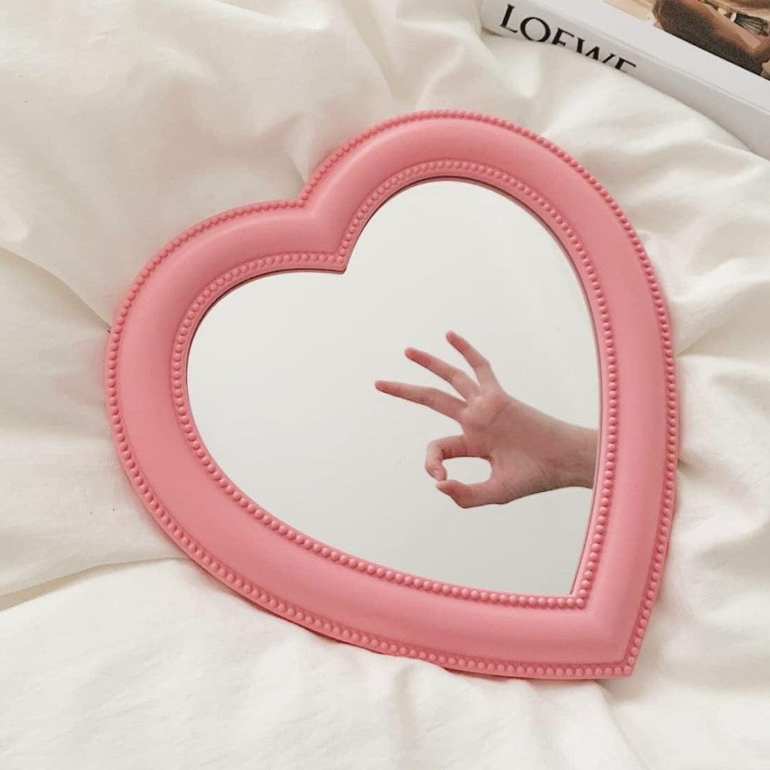 VibeCore Heart-Shaped Mirror in Pink, placed on a bed in a cozy, aesthetic bedroom, perfect for cutecore or coquette vibes. A stylish addition to any teen room or dorm room, this mirror enhances the space with its charming heart design. The soft pink color adds a gentle pop to the decor, making it ideal for anyone looking to add a trendy touch to their modern, feminine aesthetic.