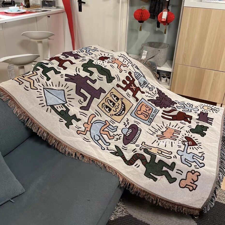 VibeCore Keith Haring Graffiti Woven Blanket on blue couch, close-up showcasing vibrant street art design and detailed 100% cotton texture.