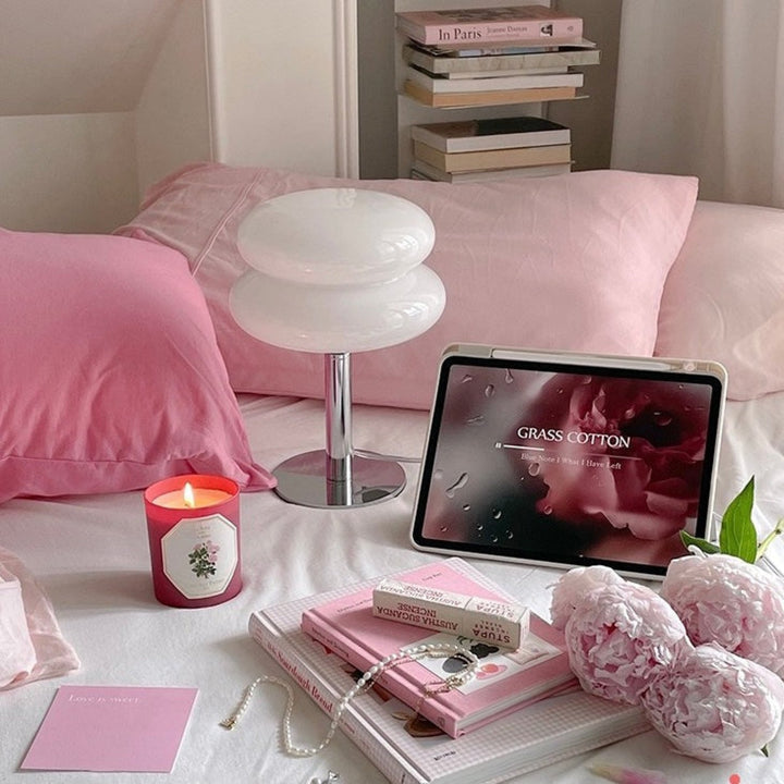 VibeCore Macarons Glass Table Lamp in white, unlit, placed on a bed, showcasing its minimalist design and soft glass finish.