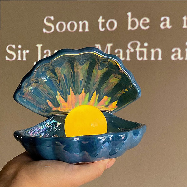VibeCore Mermaid Pearl Table Lamp in Navy Blue, featuring a glowing pearl nestled inside a beautifully crafted clam shell. Made from handmade, glazed white pottery, this lamp adds a coastal, serene vibe to your space with its soft, warm yellow glow, perfect for enhancing beach-inspired room decor.