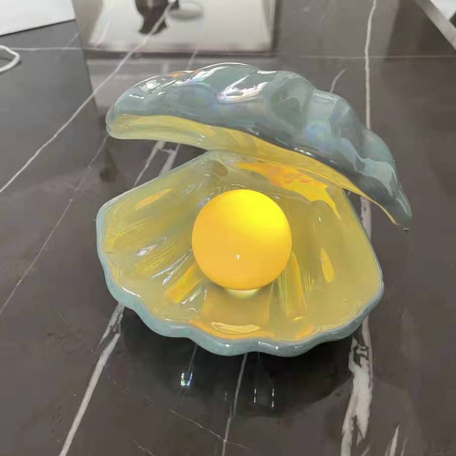 
VibeCore Mermaid Pearl Table Lamp in Pearl Blue, featuring a glowing pearl nestled inside a beautifully crafted clam shell. Made from handmade, glazed white pottery, this lamp adds coastal magic and elegance to your space with its soft, warm yellow glow. Perfect for beachy room aesthetics and adding a serene, mystical vibe to any room.