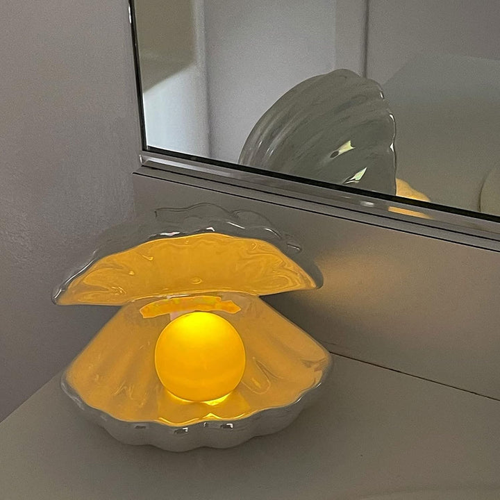 VibeCore Mermaid Pearl Table Lamp in Pearl Blue placed on a dresser, casting a soft, warm glow. The handmade glazed pottery and glowing pearl design add a coastal, serene vibe to your space, perfect for beach-inspired room decor and creating a cozy, inviting atmosphere.