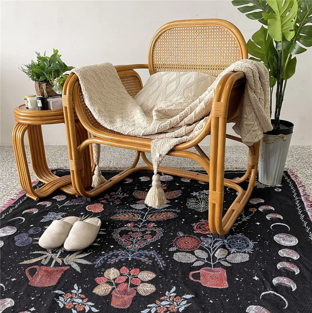 VibeCore Mystic Bloom Woven Blanket on the floor beneath a chair, showcasing its vibrant floral pattern, made from soft, 100% combed cotton for a cozy, nature-inspired aesthetic.