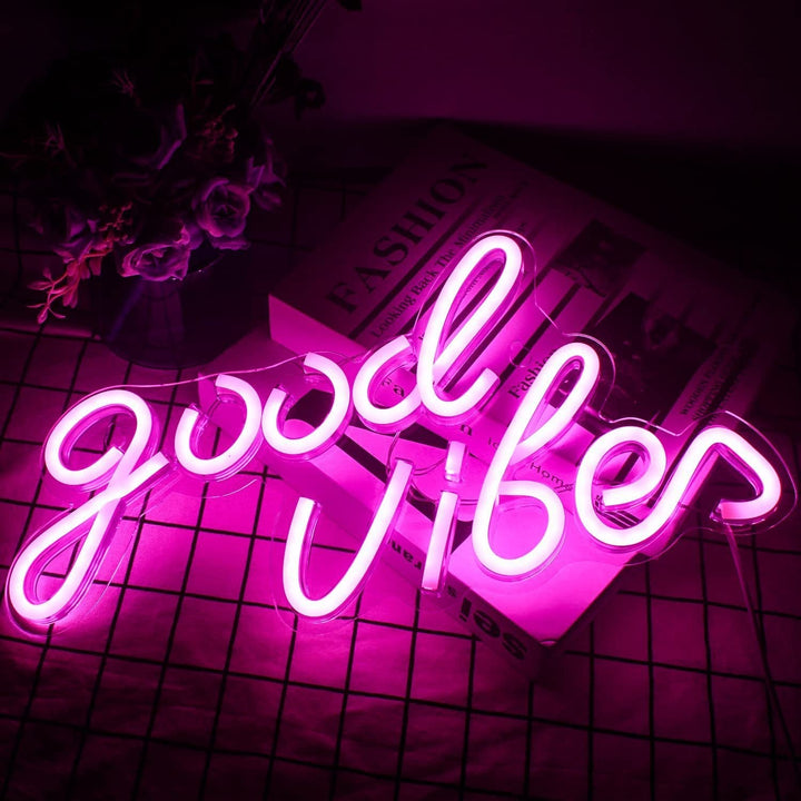 The VibeCore Pink Good Vibes Cursive Neon Light, laying on a table, adds a warm, inviting glow to your space. Perfect for creating a cozy atmosphere in bedrooms or dorms, this sign is a stylish reminder to keep the good vibes flowing.