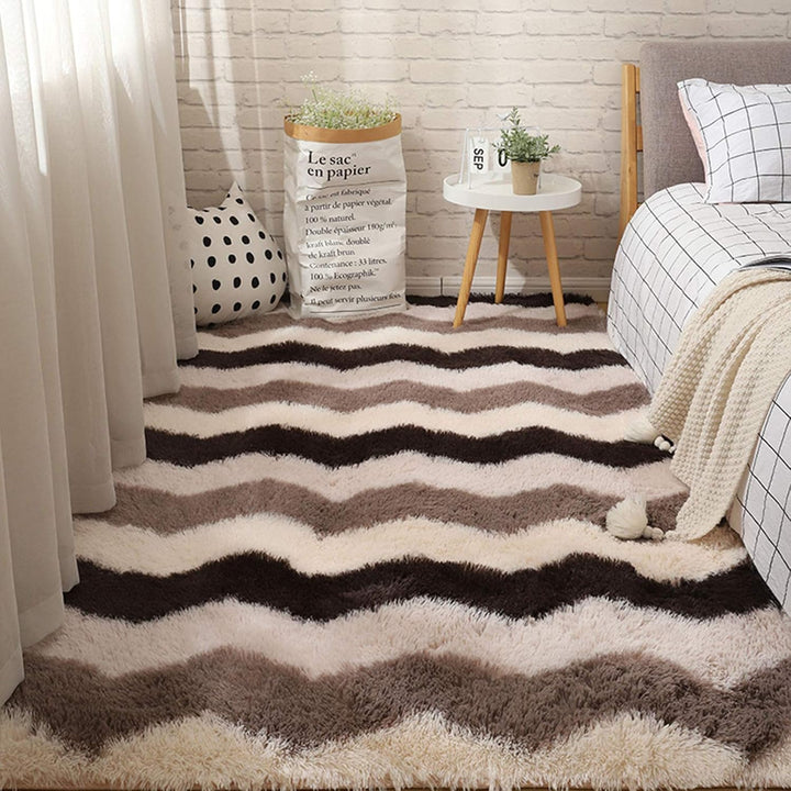VibeCore Plush Patterned Area Rug in brown zigzag pattern, placed beside a bed, featuring a soft polyester fiber texture and non-slip backing. Adds a cozy and stylish touch to your space. Easy to clean and available in 5 stylish options.