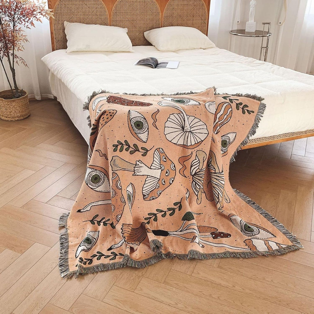 VibeCore Shroom Magic Woven Blanket draped over the corner of a bed, showcasing its dreamy mushroom pattern and soft woven texture in a cozy, ambient setting.