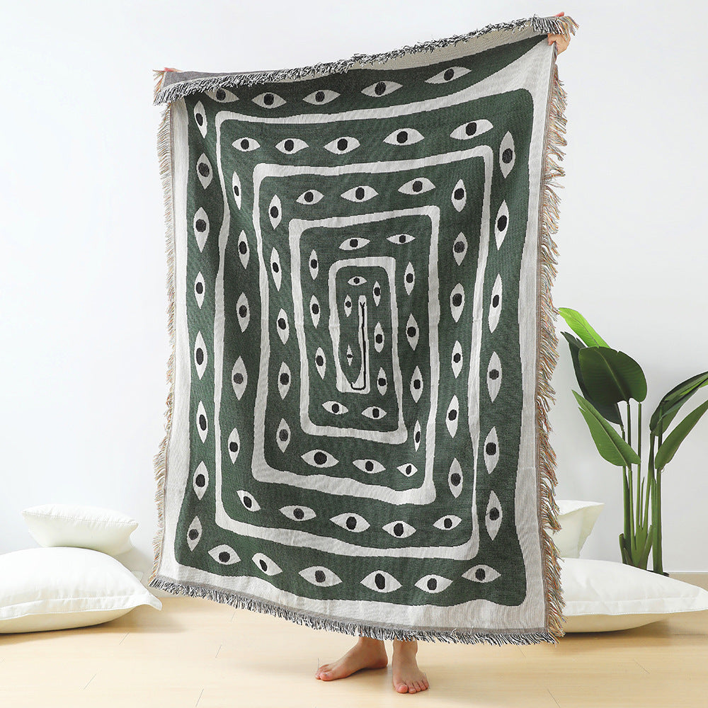VibeCore Snake-Eye Woven Blanket held up, showcasing its bold and edgy snake-eye design. Made from 100% combed cotton, this versatile piece adds a mysterious, captivating touch to your space. Perfect as a throw, wall hanging, or even a rug.