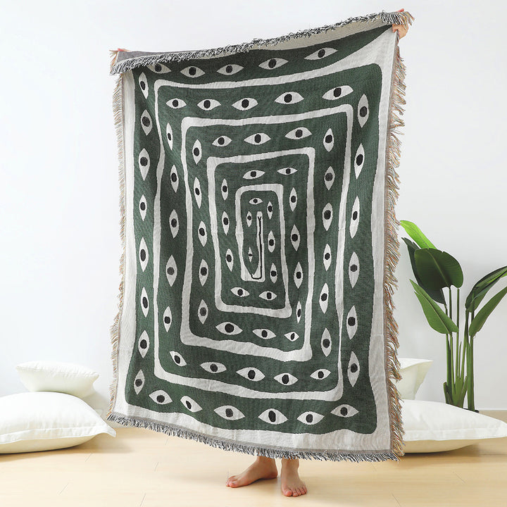 VibeCore Snake-Eye Woven Blanket held up, showcasing its bold and edgy snake-eye design. Made from 100% combed cotton, this versatile piece adds a mysterious, captivating touch to your space. Perfect as a throw, wall hanging, or even a rug.