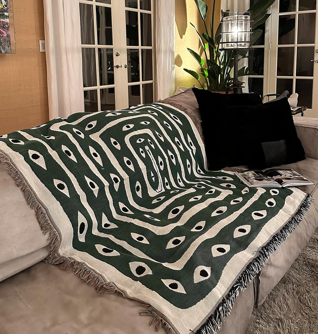 VibeCore Snake-Eye Woven Blanket draped over a couch, showcasing its bold snake-eye design. Made from 100% combed cotton, this versatile blanket adds a captivating, mysterious touch to your living space.