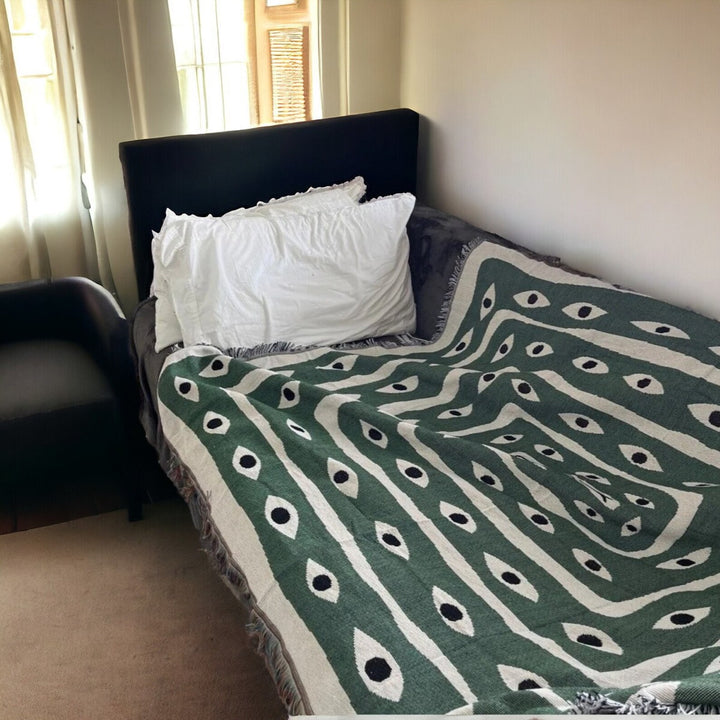 VibeCore Snake-Eye Woven Blanket draped over a sofa, showcasing its striking snake-eye design. Crafted from 100% combed cotton, this versatile blanket adds a bold, mysterious vibe to your living space while providing comfort and style.