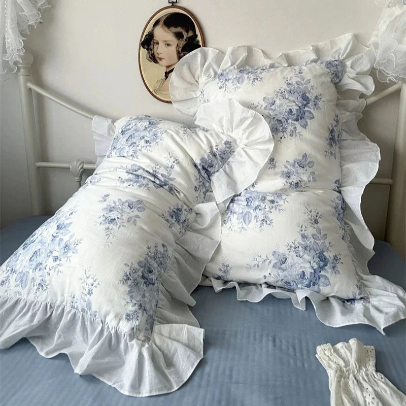 Floral patterned pillows with ruffles on a bed, white canopy, and portrait in the background.