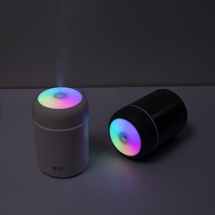 The white and gray diffusers softly glowing with mist in a dark setting, casting a peaceful atmosphere with their LED lights and gentle mist.